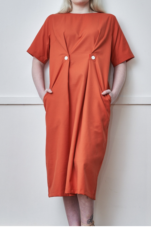 Woman wears orange dress with decorative buttons and pockets